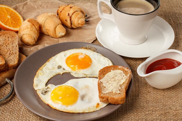 Plate with fried eggs and toast with butter croissants and bread