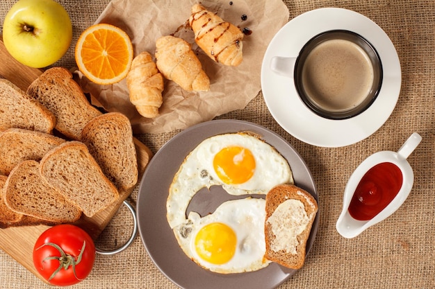 Plate with fried eggs and toast with butter cup of coffee croissants and bread