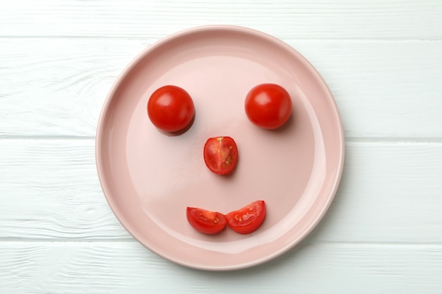 Plate with happy face made of tomato on white wooden