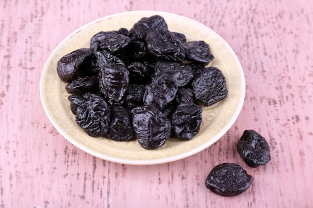 Plate with heap of prunes on color wooden background