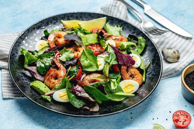 Plate with a keto diet food menu with cherry tomatoes, cucumber, avocado, eggs and smoked shrimps, mixed greens. Healthy food. Clean eating.