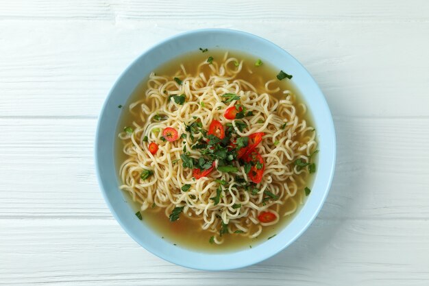 Plate with noodles soup on white wooden background