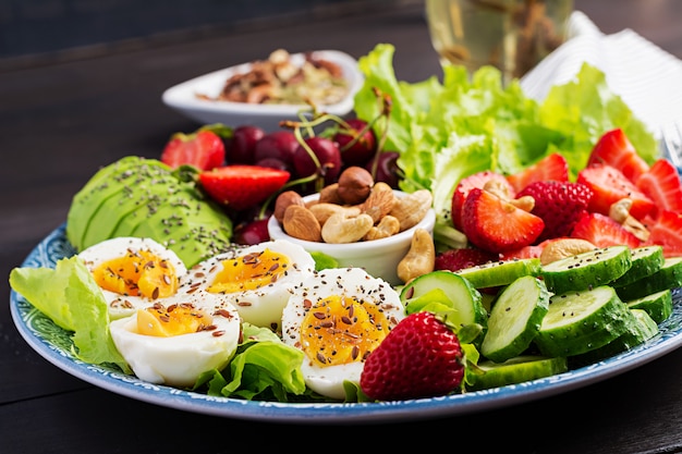 Plate with a paleo diet food, Boiled eggs, avocado, cucumber, nuts, cherry and strawberries, Paleo breakfast.