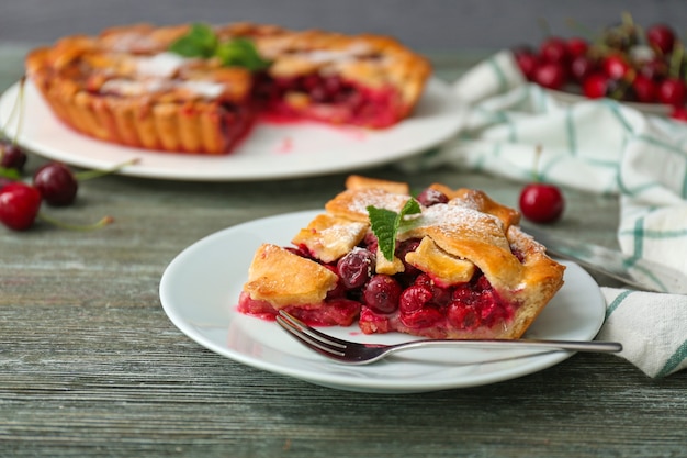 Plate with piece of delicious cherry pie on wooden table