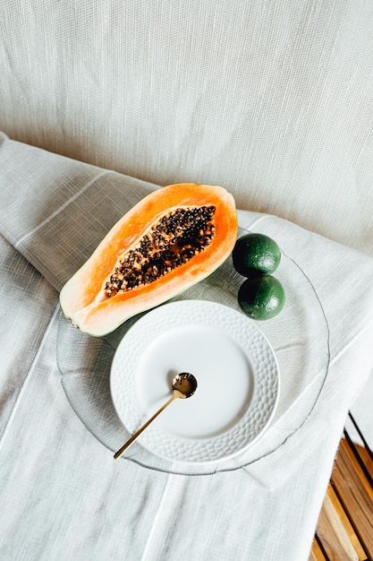 A plate with a piece of fresh papaya on it cut in half on a plate with two limes Minimalism background natural concept