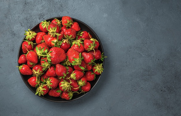 A plate with ripe strawberries on a dark blue background. Top view, copy space.