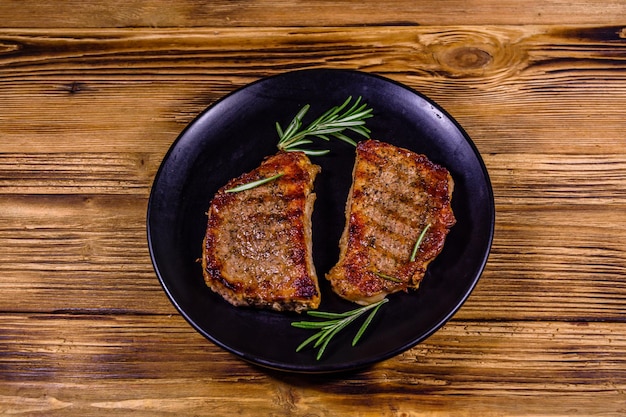 Plate with roasted steaks and rosemary twigs on a wooden table