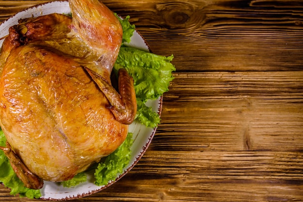 Plate with roasted whole chicken and lettuce leaves on a wooden table Top view