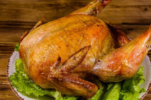 Plate with roasted whole chicken and lettuce leaves on a wooden table