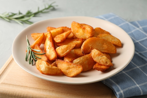 Plate with slices of baked potato wedges, napkin on gray. Closeup