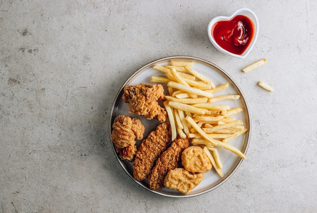 Plate with snacks on stone background nuggets wings strips and fries with ketchup top view with copy space