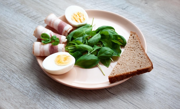 Plate with spinach leaves green basil bacon eggs and a piece of rye bread Food for breakfast