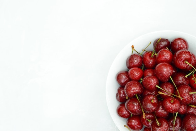 Plate with sweet cherry berries on white background top view Many ripe red berries in white plate