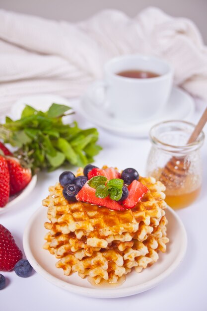 Plate with sweet tasty waffles with honey, berries, cup of tea