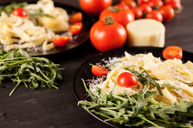 Plate with tagliatelle pasta, cherry tomatoes and greenery on wooden table