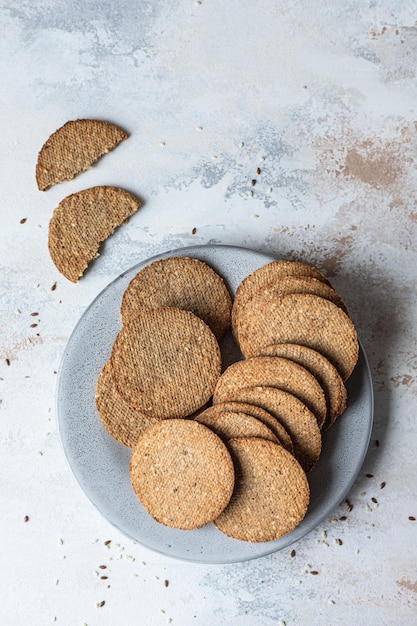 Plate with tasty crackers with sesame and flax seeds on grey stone background. Top view.