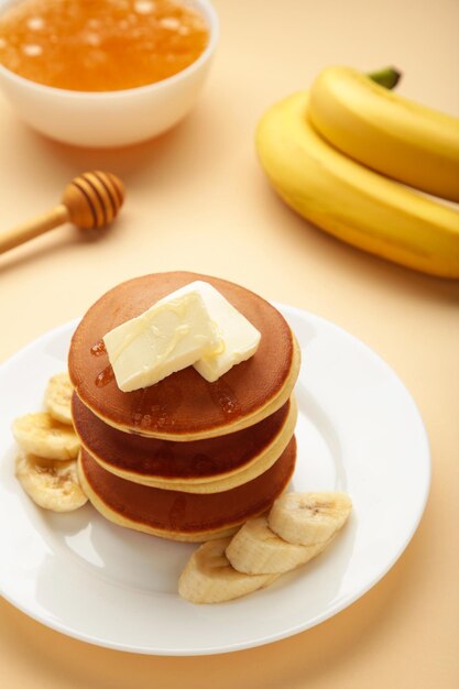 Plate with yummy banana pancakes on beige background Vertical photo