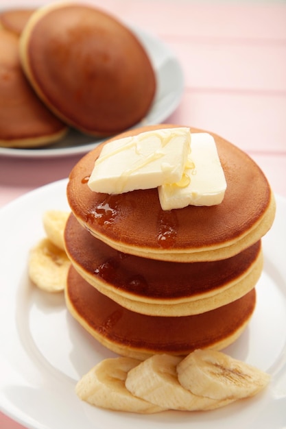 Plate with yummy banana pancakes on pink background Vertical photo