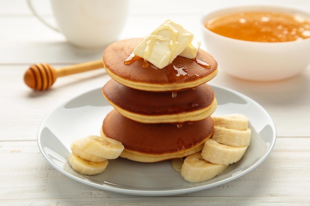 Plate with yummy banana pancakes on white background