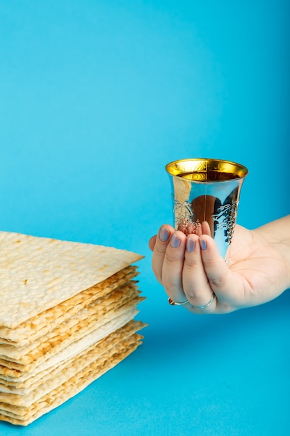 Plates of matzo laid on top of each other on a blue surface and a glass of kiddush wine in hand