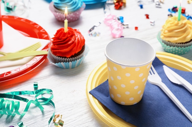 Plates with birthday cupcakes and cups on wooden table