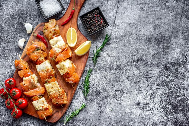 A platter of salmon skewers with lemons and garlic on a dark background.