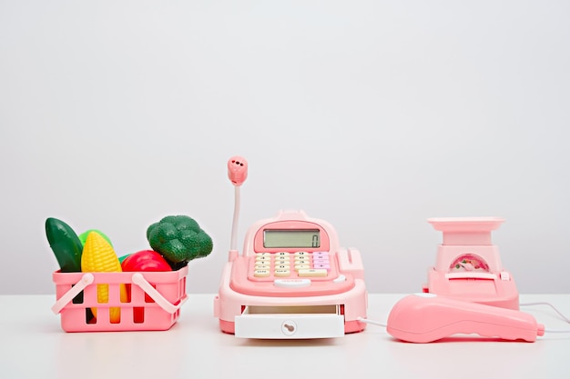 Play store plastic children's toy vegetables in pink basket cash register scales on white background online ordering of products from store