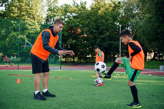 Player in football uniform working out the kicking ball with coach on stadium