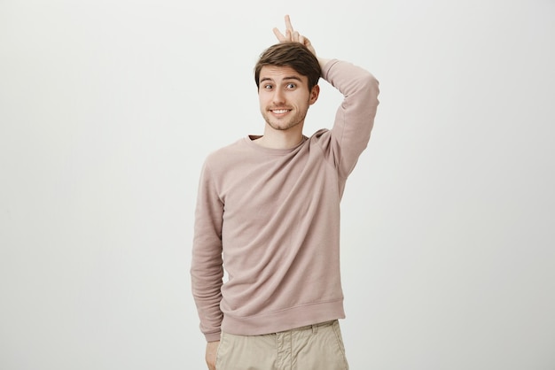 Playful charming european student holding victory or peace sign behind head as if it is horns