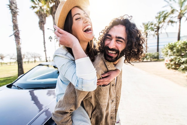 Playful couple of lovers having piggyback ride near the car