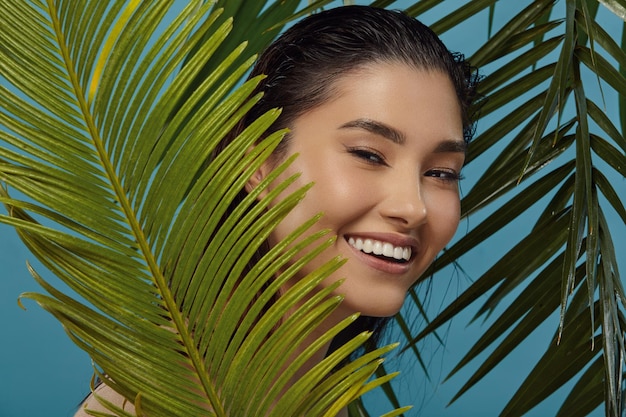 Playful girl peeks out from behind palm leaves smiles