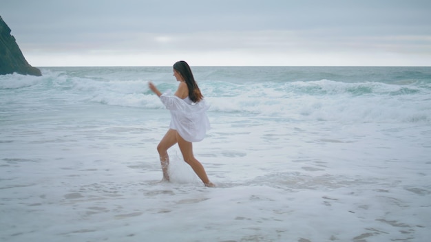 Playful girl running sea waves enjoying cloudy weekend woman jumping on beach