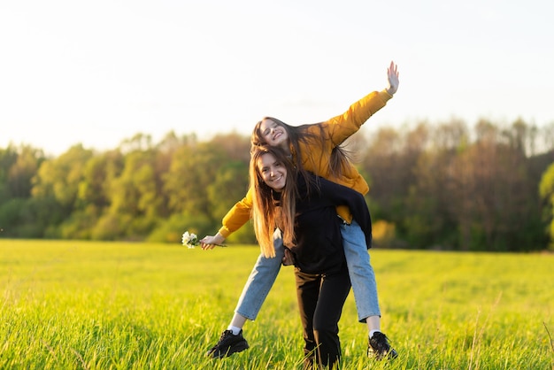 Playful mother giving daughter piggy back ride at green field