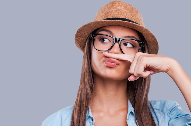 Playful style. Close-up portrait of a young woman holding a finger up to her nose while looking away