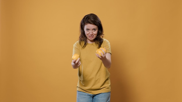 Playful woman acting silly trying to juggle oranges being funny while dropping them in studio. Individuality concept of person with fun and goofy personality showing juggle talent.