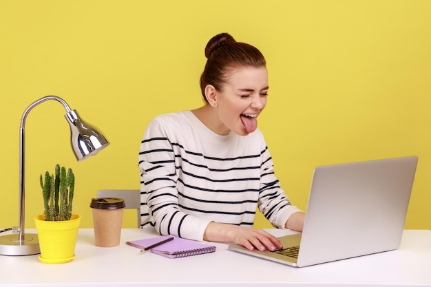 Playful woman office worker in striped shirt showing tongue out expressing positive childish emotion