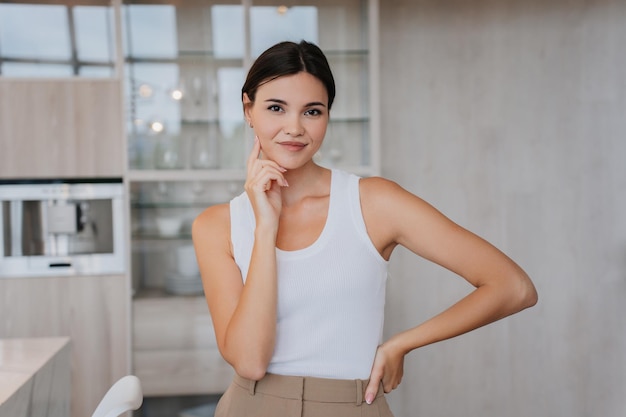 Playful young asian woman in white tshirt and beige pants over blurry living room Pretty Korean model touching her face with perfect skin looks at camera smiling Fit female home Beauty and health