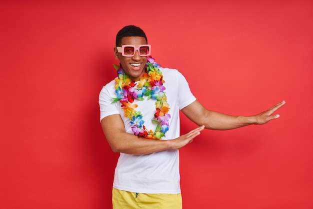 Playful young man in hawaiian necklace dancing against red background