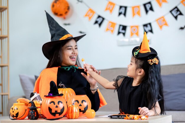 Playful young mother sitting on comfy couch in living room with cute little daughter tells spooky