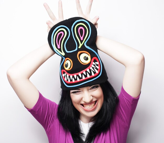 Playful young woman in funny hat with rabbit, studio shot