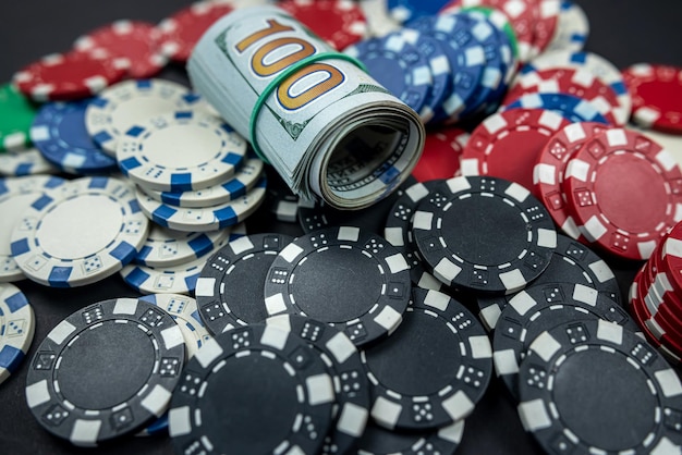 Playing cards scattered with chips behind a roll of us dollars isolated on background