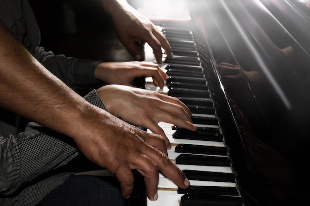 Playing four male hands on the piano. palms lie on the keys and play the keyboard instrument in a music school. student learns to play. hands of a pianist. black dark background.