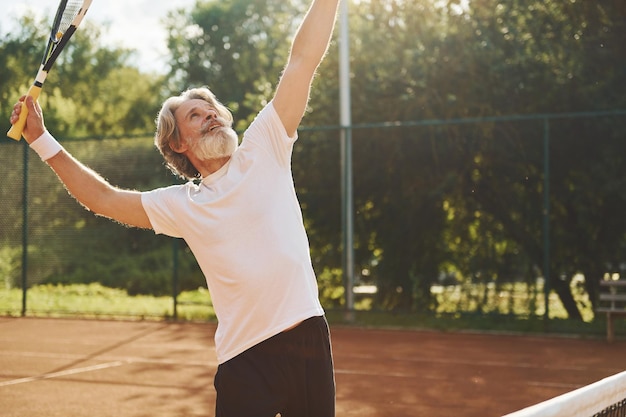 Playing game Senior modern stylish man with racket outdoors on tennis court at daytime