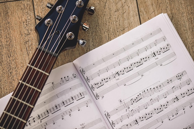 Playing guitar closeup photo of guitar neck and music notes against of wooden background