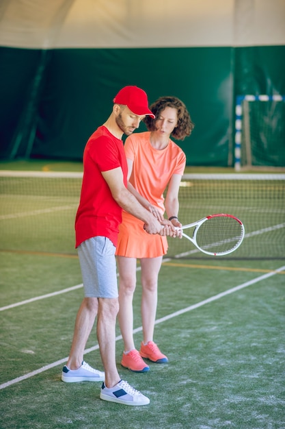 Playing tennis. Man in a red cap and with a racket having a workout with his female coach