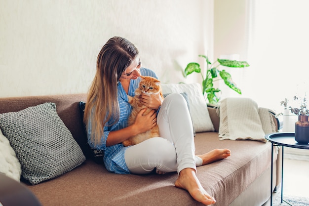 Photo playing with cat at home. young woman sitting on couch with pet.