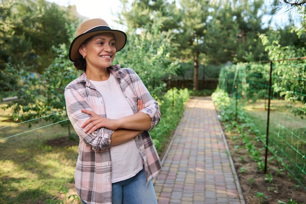 Pleasant amateur farmer gardener standing near a row of planted seedlings in her organic farm on sunny spring day