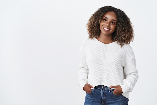 Pleasant and charismatic african-american young woman tilting head casually and smiling broadly holding hands in pockets