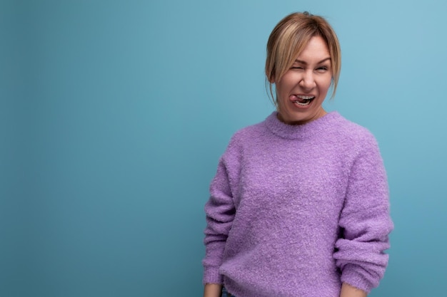 Pleasant charming cute blond young woman consultant in purple sweater makes a face on a blue