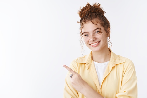 Pleasant charming happy redhead daughter cute freckles showing mom campus pointing left moving new appartment give short room-tour smiling happily indicating sideways, white background